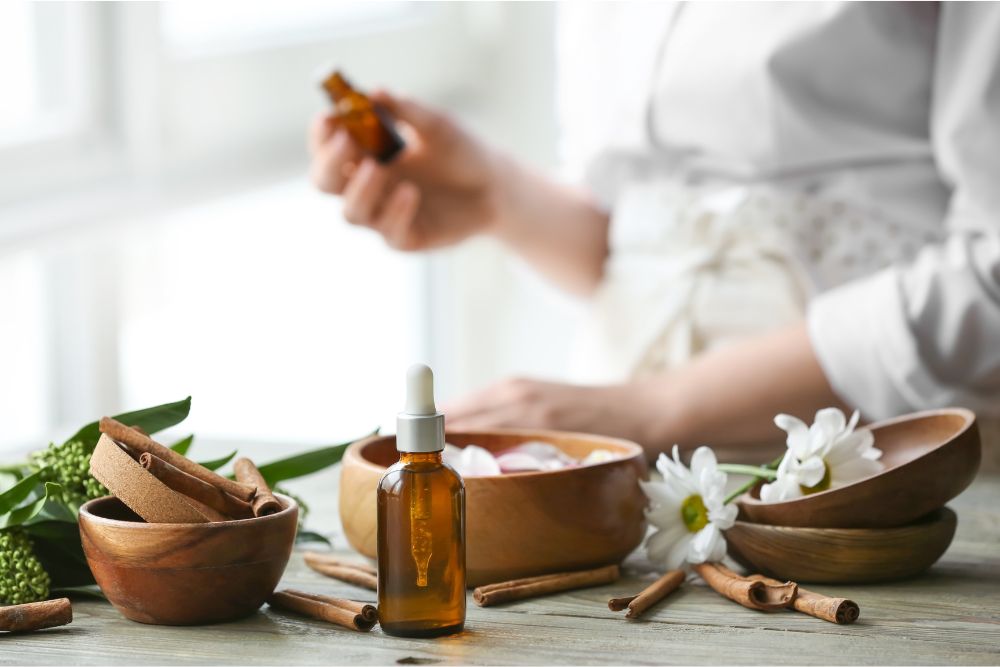 Glasfläschchen mit ätherischen Ölen umgeben von frischen Kräutern und Blüten