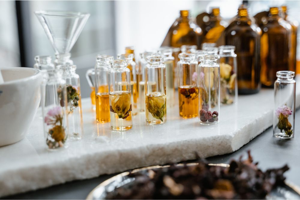 Gläser mit verschiedenen ätherischen Kräuterölen und frischen Kräutern auf Holzuntergrund – natürliche Aromatherapie