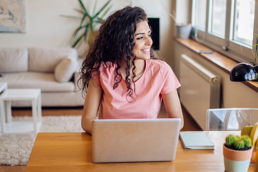 Lächelnde Frau am Laptop im Home-Office, Symbol für Zufriedenheit und Wohlbefinden dank Aromatherapie bei der Arbeit