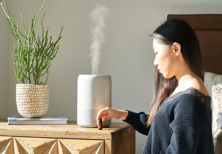 Frau träufelt ätherisches Öl in einen Aroma-Diffuser als Teil der Vorbereitung auf einen ruhigen Schlaf.