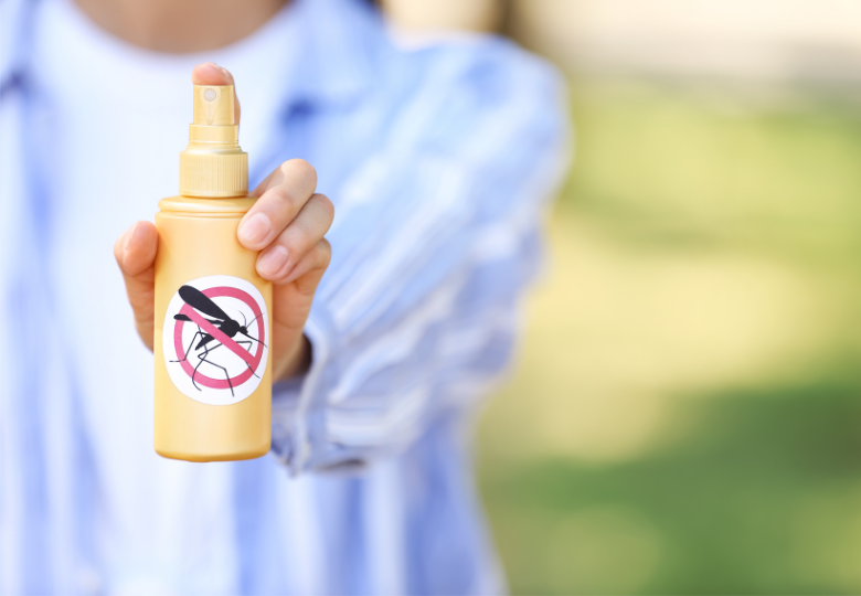 Person, die ein Mückenschutzspray im Freien hält.